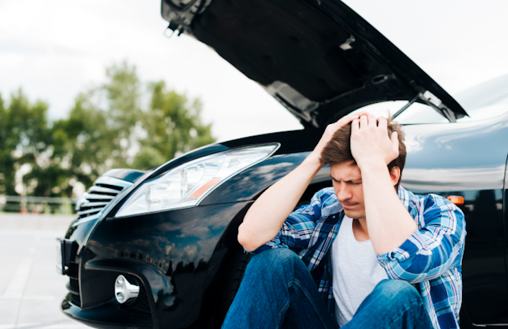 Hombre lamentándose con coche roto detrás